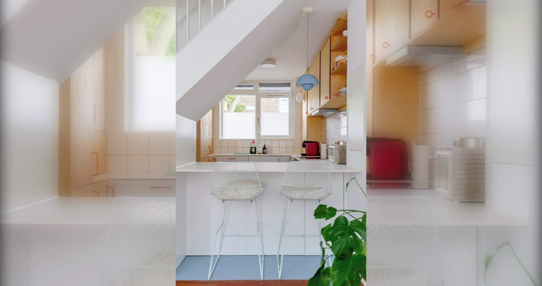 A modern kitchen with white cabinetry, a central island with bar stools, and a staircase leading to an upper level.