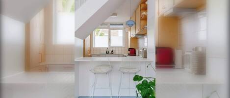 Une cuisine moderne avec des meubles blancs, un îlot central doté de tabourets de bar et un escalier menant à un niveau supérieur.