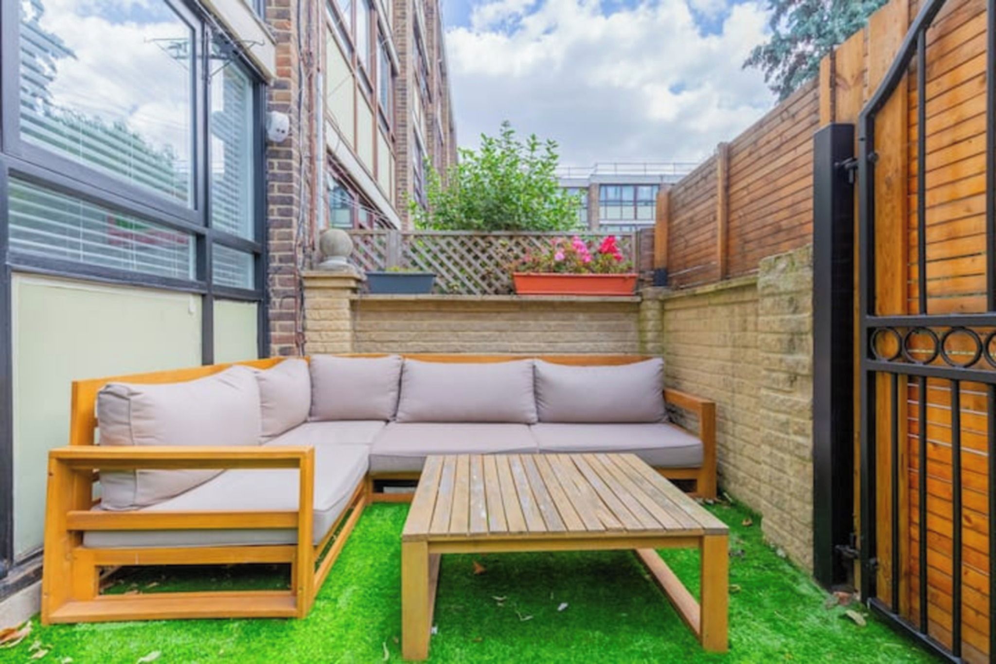 A small outdoor patio with a wooden bench, a wooden table, and a beige sectional sofa.