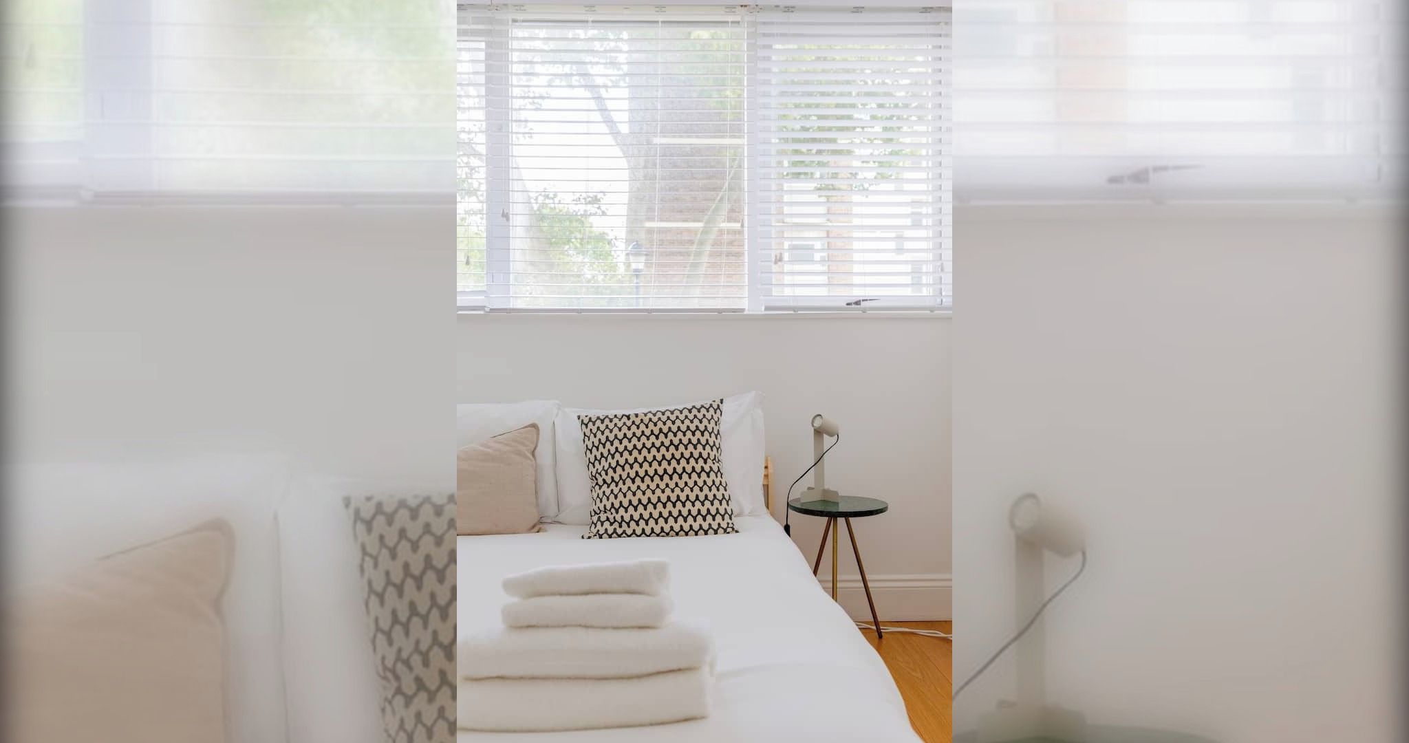 Une chambre à coucher avec un lit, des oreillers, une table de chevet et une fenêtre avec des stores.