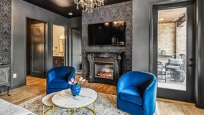 Un salon moderne avec une cheminée, deux fauteuils bleus, une table basse ronde et un lustre.