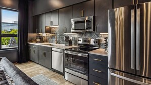 Une cuisine moderne dotée d’appareils électroménagers en acier inoxydable, de meubles de rangement aux couleurs sombres et offrant une vue sur la verdure environnante.