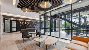 Un hall d’hôtel moderne comprenant un comptoir d’accueil, un espace salon et un escalier menant aux étages supérieurs.
