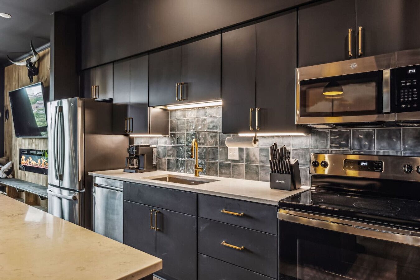 Modern and stylish open-concept kitchen and living area. The kitchen features dark cabinets, a sleek white countertop, and contemporary bar stools.