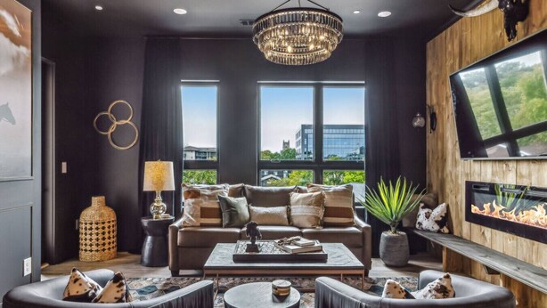 Un salon moderne avec un grand canapé, deux fauteuils, une table basse et un téléviseur fixé au mur.