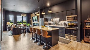 Une cuisine moderne avec des meubles de couleur sombre, des appareils en acier inoxydable et un îlot central doté de tabourets de bar.