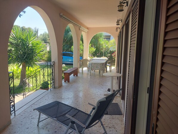 A covered outdoor area with a table and chairs, a bench, and a glass table with chairs. - 110 m² House in Kakovatos - Peloponnese (zacharo)