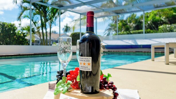 Une bouteille de vin, un verre et une grappe de raisins sur une table près d’une piscine.