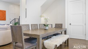 A dining area with a wooden table, six chairs, and a bench. There is a white door and a staircase in the background.