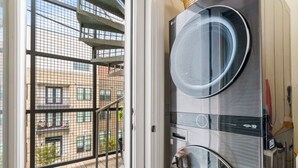A modern apartment with a balcony, a washing machine, and a view of a building with balconies.