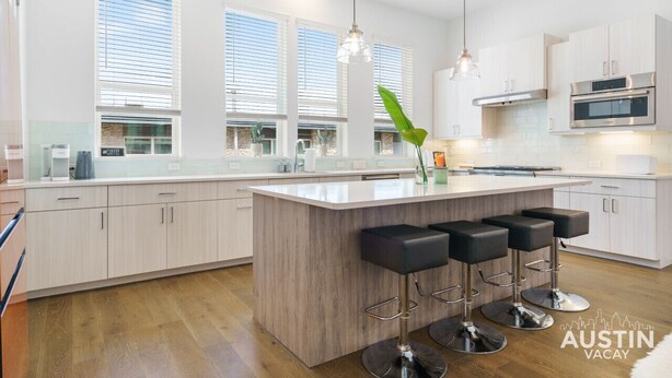A modern kitchen with a central island, bar stools, and a large window with blinds.