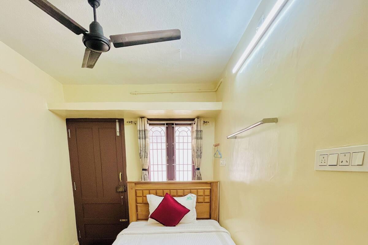 Ein Schlafzimmer mit einem hölzernen Bett, einem Deckenventilator, einem Fenster mit Vorhängen und einer Tür.