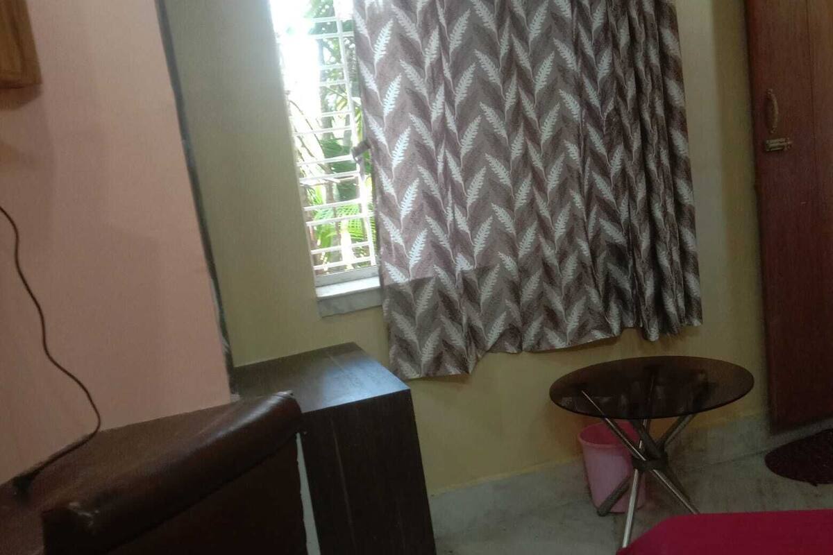 A room with a window, a curtain, a table, and a bed.