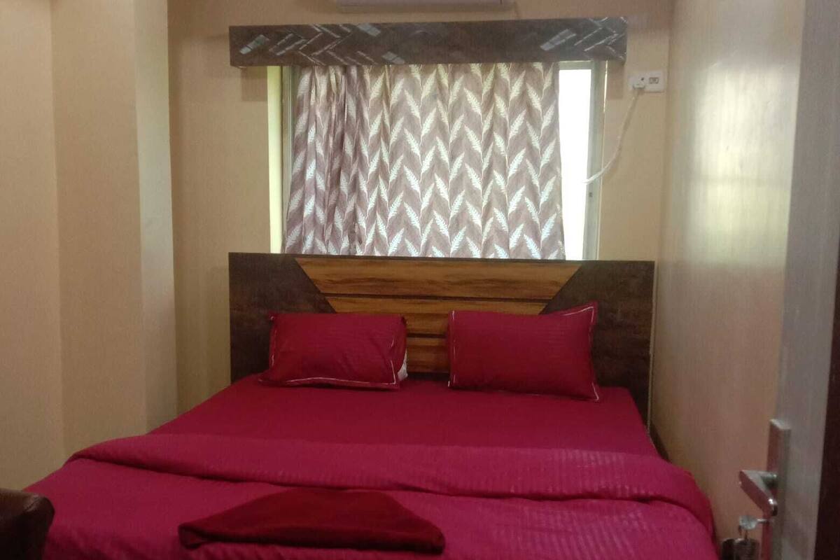 A bedroom with a wooden headboard, a bed with red bedding, and a window with patterned curtains.