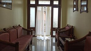 Ein Zimmer mit einer Sofagarnitur, einem Esstisch mit Stühlen, einem großen Fenster mit Vorhängen und Wandspiegeln.