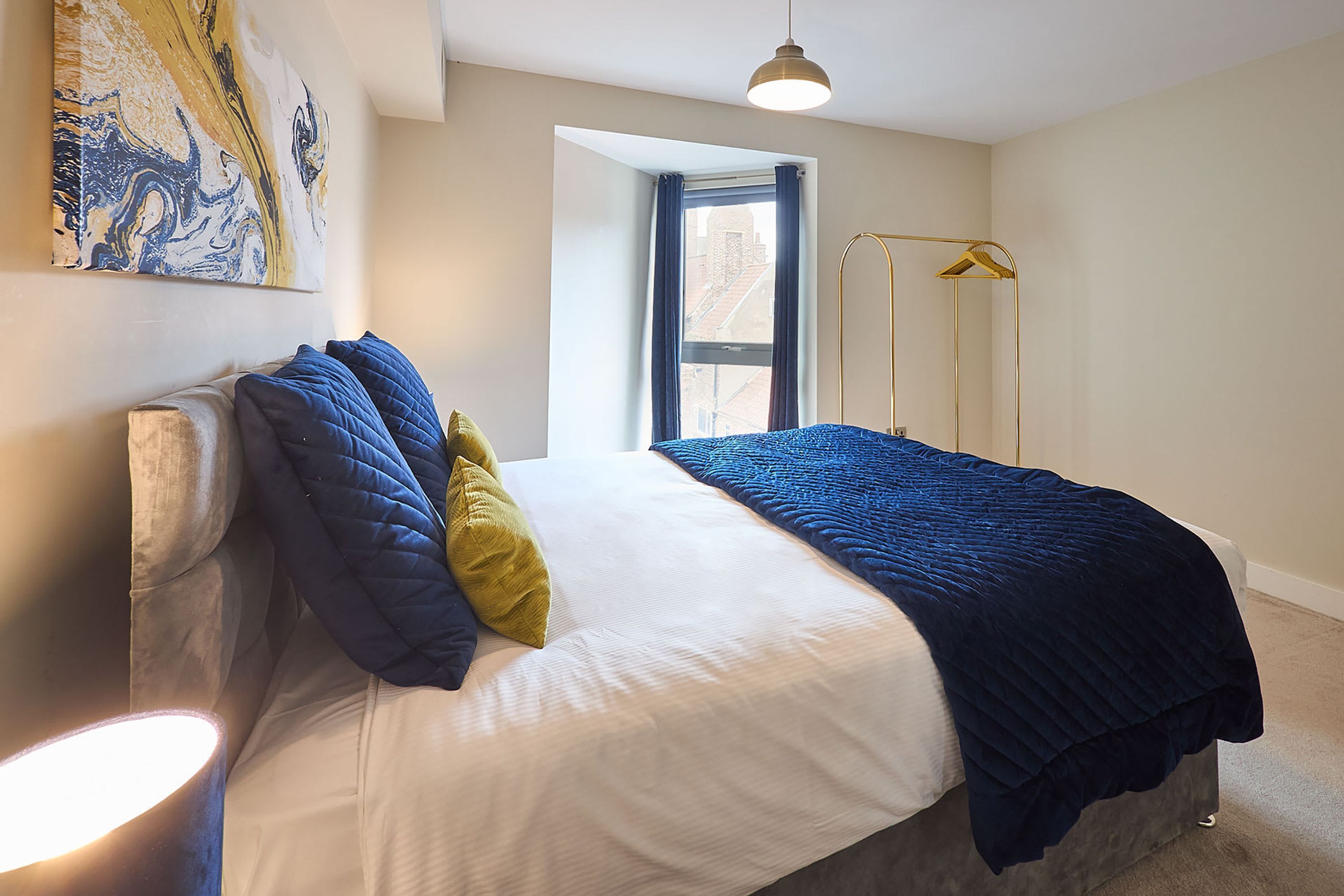 A bedroom with a bed, pillows, a bedside lamp, a floor lamp, and a window with curtains.