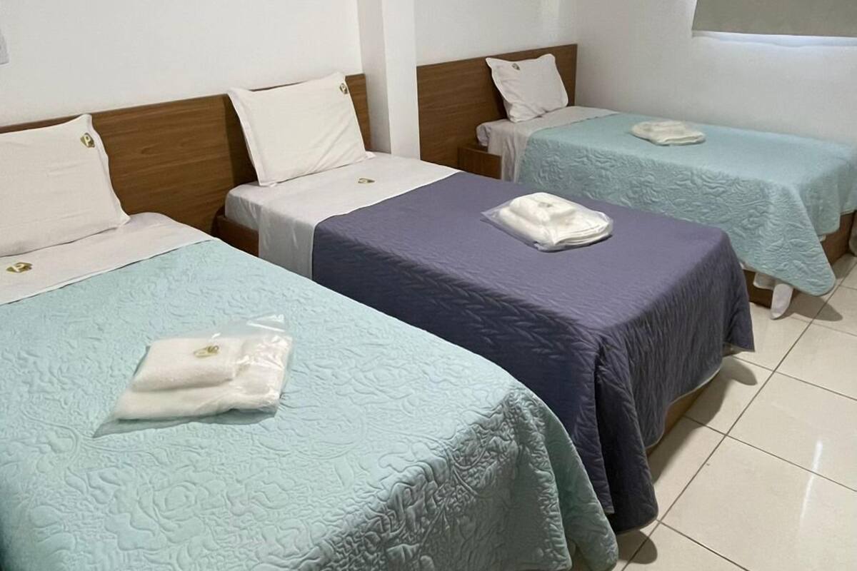 A hotel room with three beds, each with a different colored bedspread and pillows.