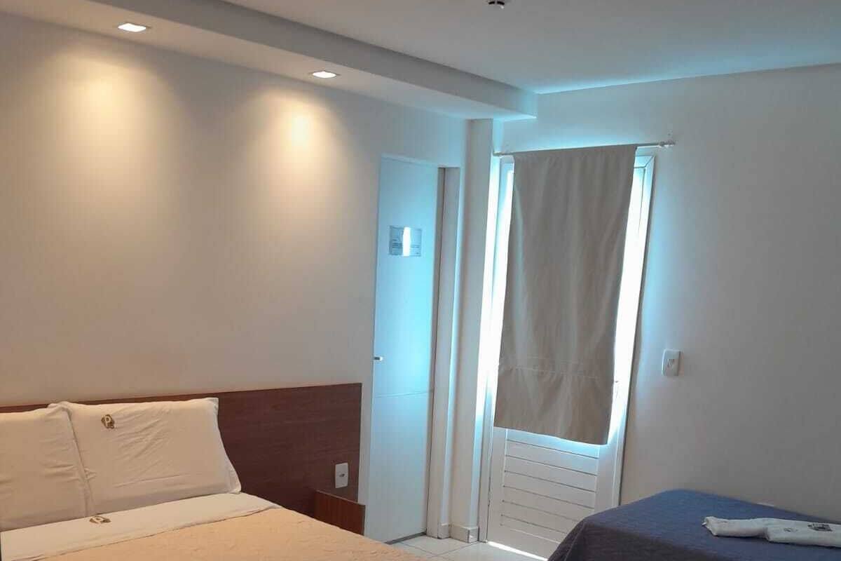 A hotel room with a large bed, a smaller bed, a window with curtains, and a door.