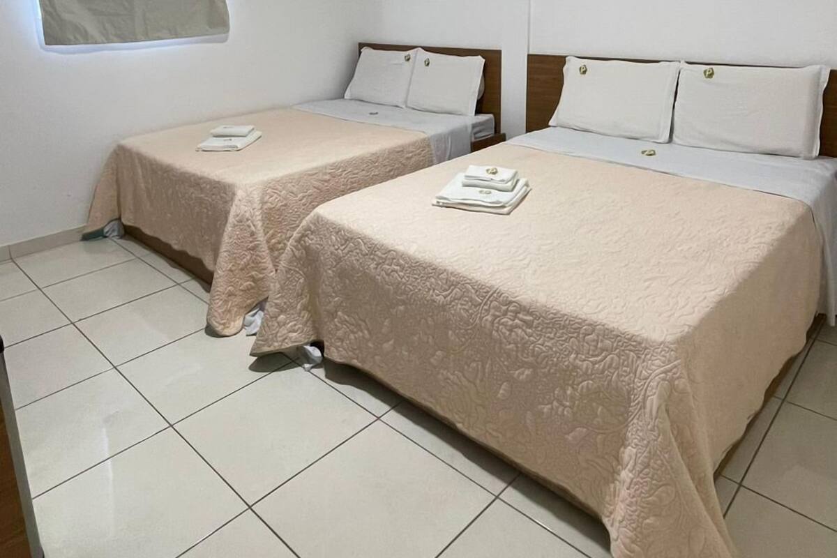 A hotel room with two beds, a window with curtains, and a tiled floor.