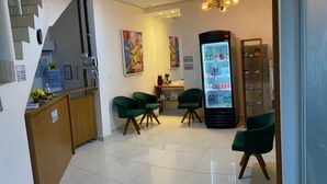 A reception area with a counter, green chairs, a refrigerator, and a staircase. - Hotel Prime Suítes (Cupira)