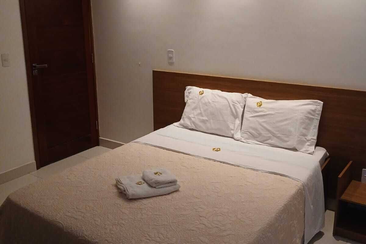 A neatly made bed with a beige bedspread and two pillows, a wooden headboard, and a small bedside table with a lamp.