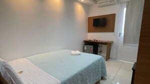 A hotel room with a bed, a desk, a television mounted on the wall, and an air conditioning unit. - Hotel Prime Suítes (Cupira)