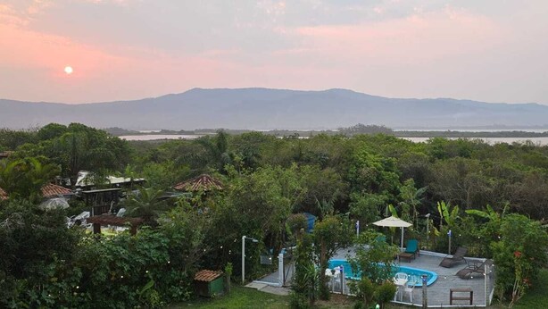 A resort with a swimming pool, lush greenery, and a view of distant mountains. - Pousada Jardim da Lagoa (Garopaba)