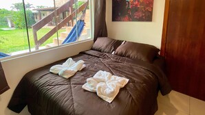 A bedroom with a large bed, a window with a view of a staircase and greenery, and a painting on the wall. - Pousada Jardim da Lagoa (Garopaba)
