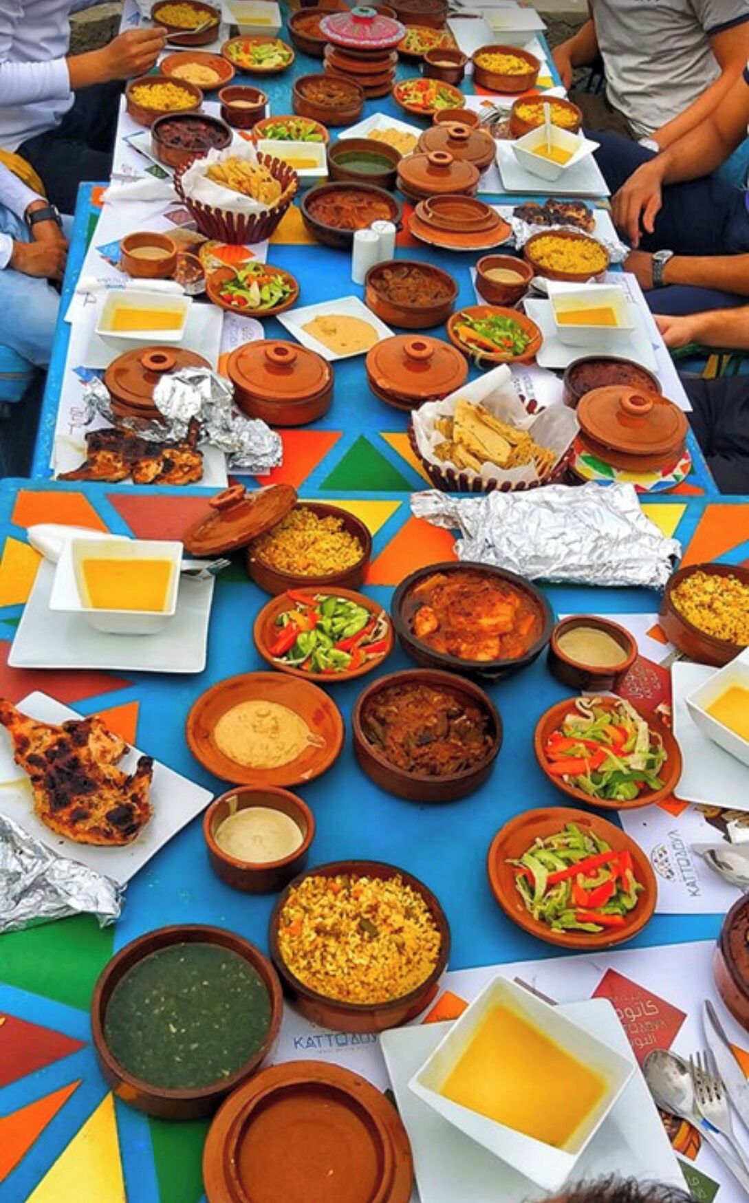 Une table où sont disposés divers plats et aliments, notamment des bols, des assiettes et des aliments emballés dans du papier d’aluminium.