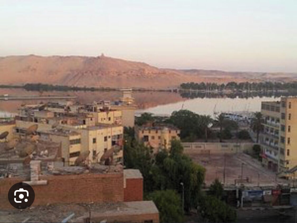 A cityscape with buildings, a river, and a hill in the background.