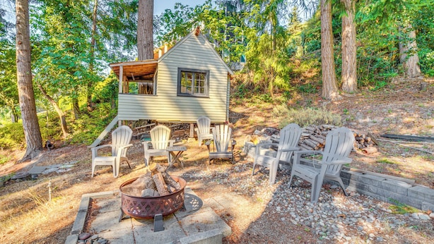 A cabin with a deck, surrounded by trees, and furnished with chairs and a fire pit. - Gig Harbor Home: Large Deck, Outdoor Dining Area (Gig Harbor)