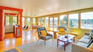 A spacious living room with a large window, a dining area, and a kitchen. - Gig Harbor Home: Large Deck, Outdoor Dining Area (Gig Harbor)