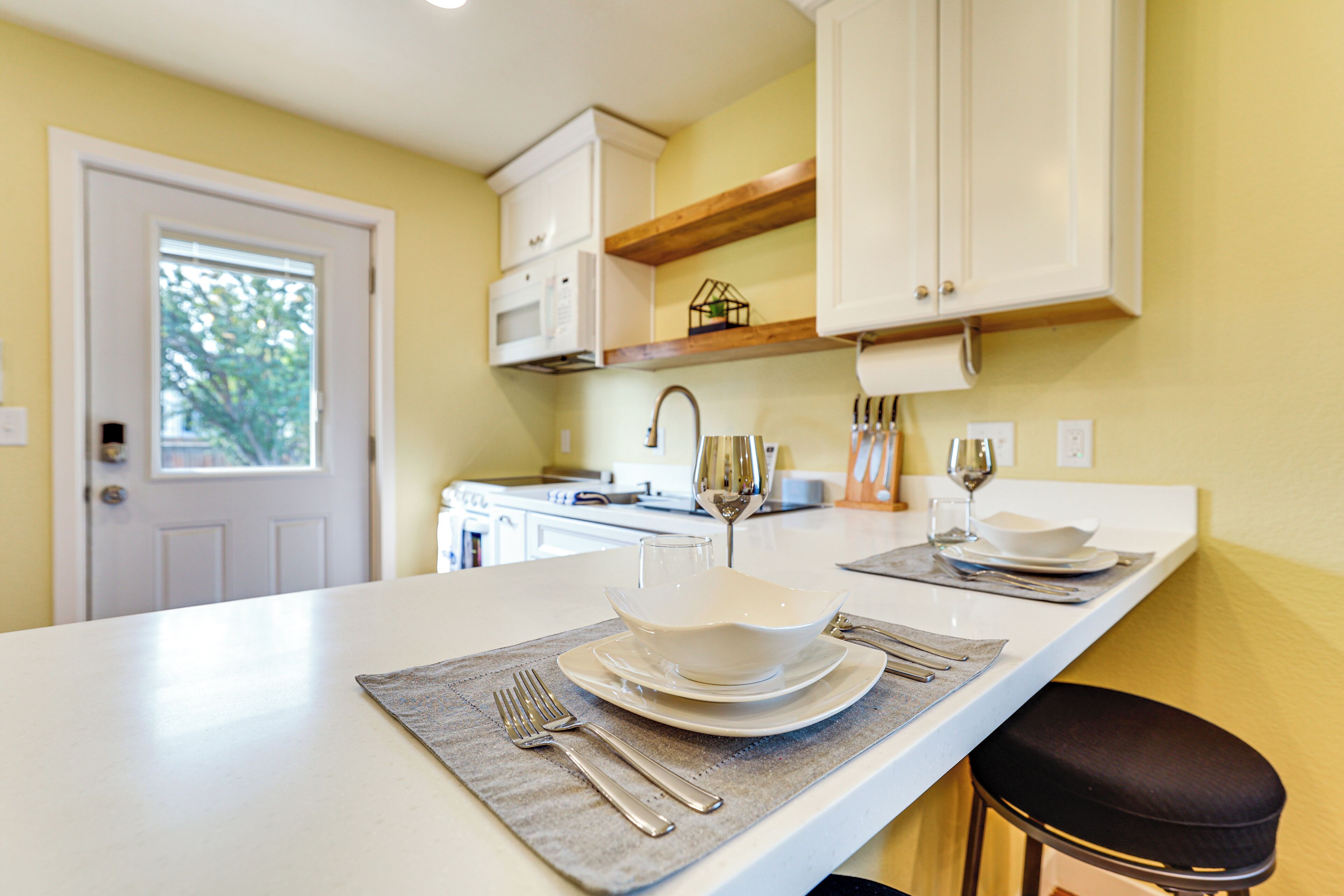 A modern kitchen with white cabinets, a countertop, and a dining area set with plates, cutlery, and glasses.