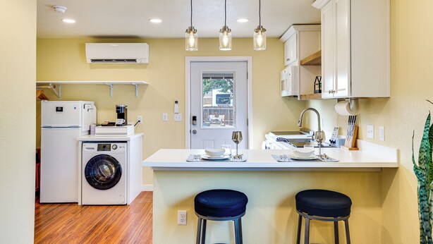 A compact kitchen with a washing machine, a coffee maker, and a sink. There are two stools at the counter. - Modern Studio Near Lake Lowell: 6 Mi to Boat Ramp (Nampa)