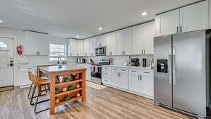 A modern kitchen with white cabinets, stainless steel appliances, and a wooden island with bar stools. - 1 Mi to MGM Springfield: Cozy Winter Duplex! (Springfield)