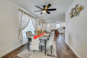 A dining area with a table set for four, a ceiling fan, and a kitchen in the background.