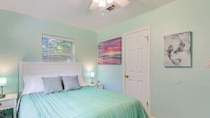 A bedroom with a bed, nightstands, a door, and wall art. - Emerald Coast Home: Outdoor Entertainment Area! (Mary Esther)