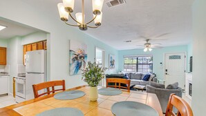 A dining area with a wooden table, chairs, and a vase of flowers. There is a kitchen in the background with a refrigerator and cabinets. - Emerald Coast Home: Outdoor Entertainment Area! (Mary Esther)