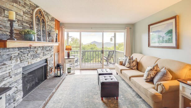 A living room with a stone fireplace, a beige sofa, and a balcony with a view of mountains. - 1 Mi to Ski Lifts: Sugar Mountain Condo (Banner Elk)