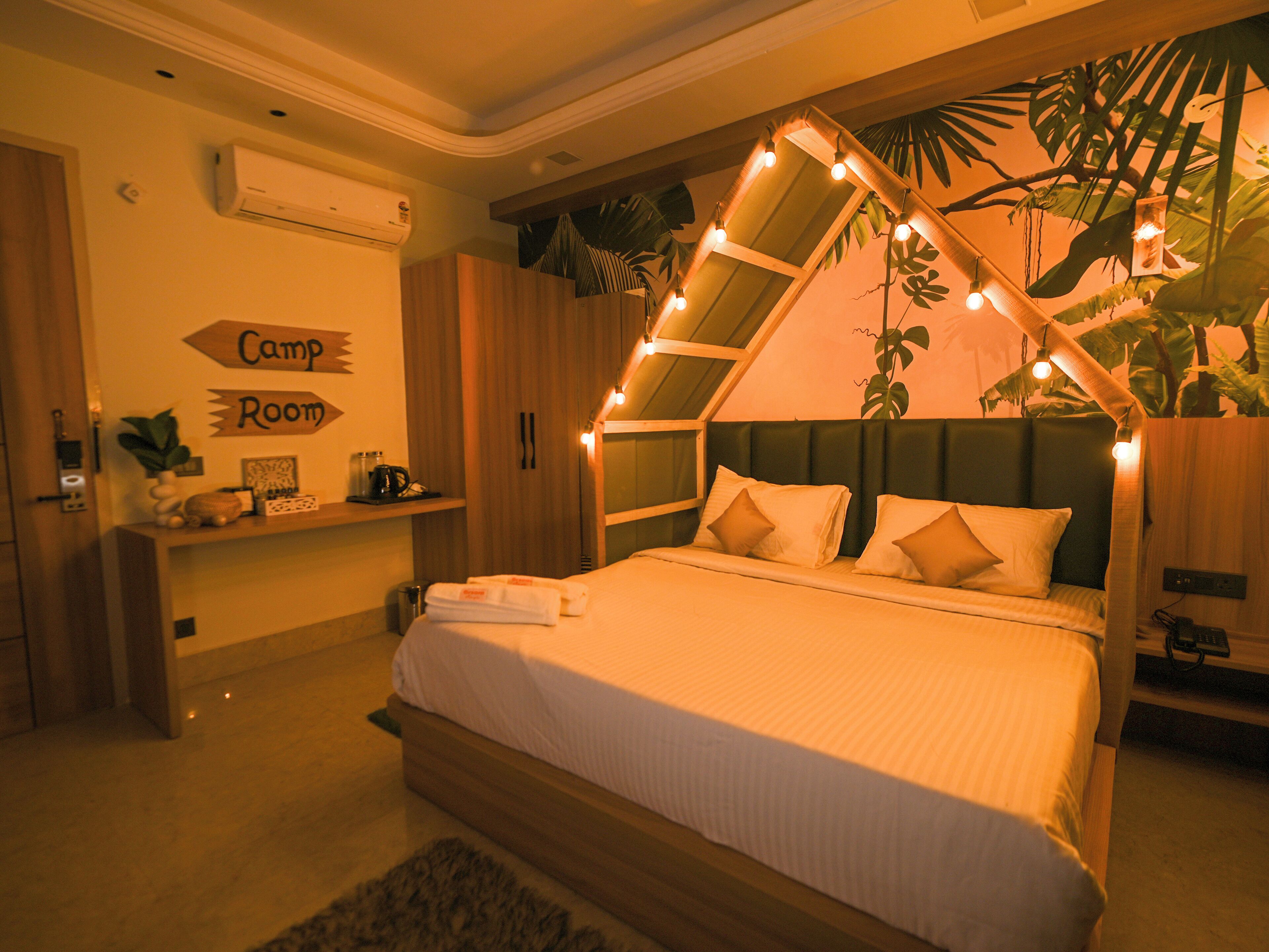 Un dormitorio con cama, mesita de noche, aire acondicionado de pared, estante con adornos y un letrero que dice "Camp Room".