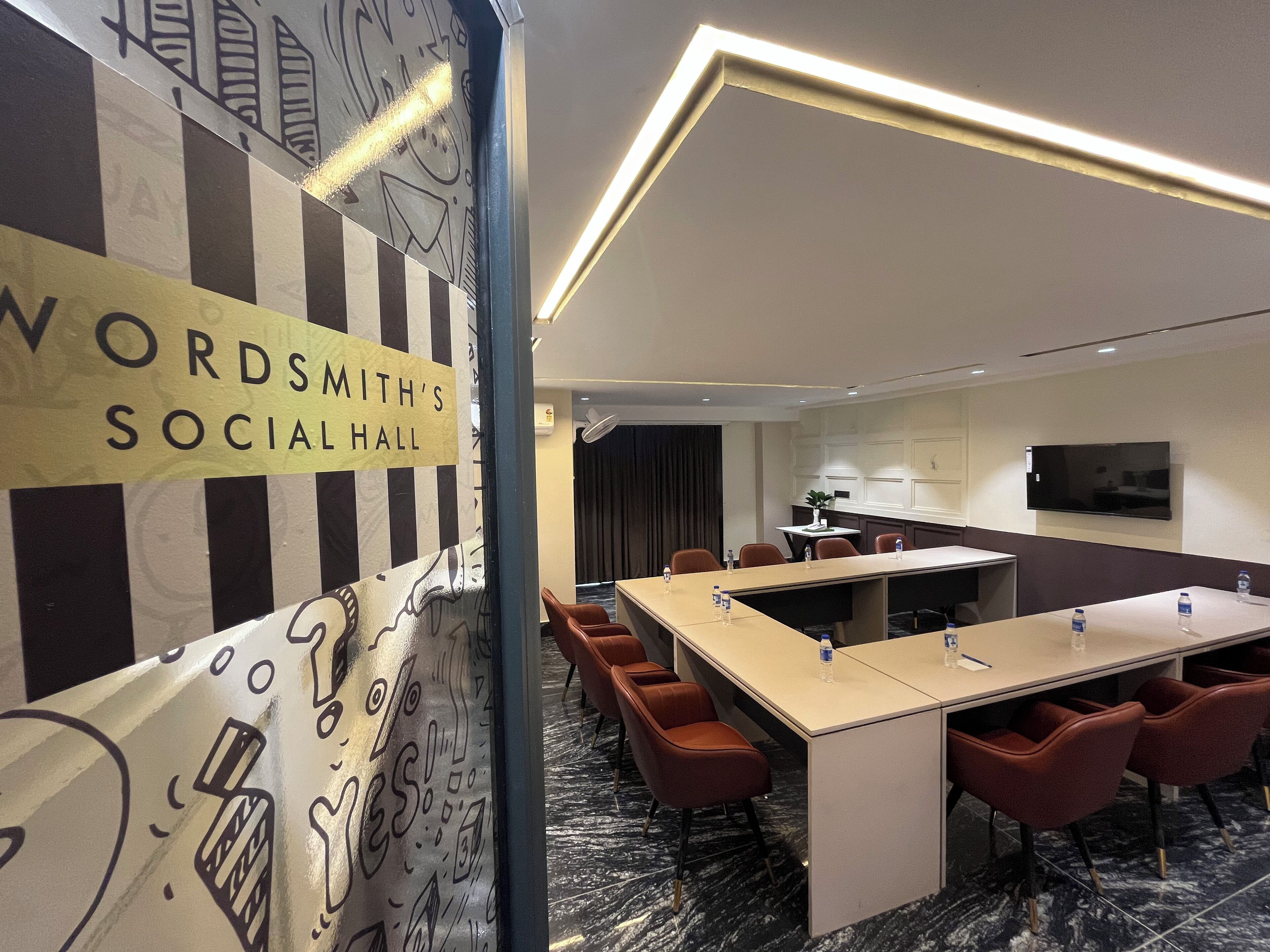 A conference room with a long table, red chairs, and a sign reading "WORDSMITH'S SOCIAL HALL".