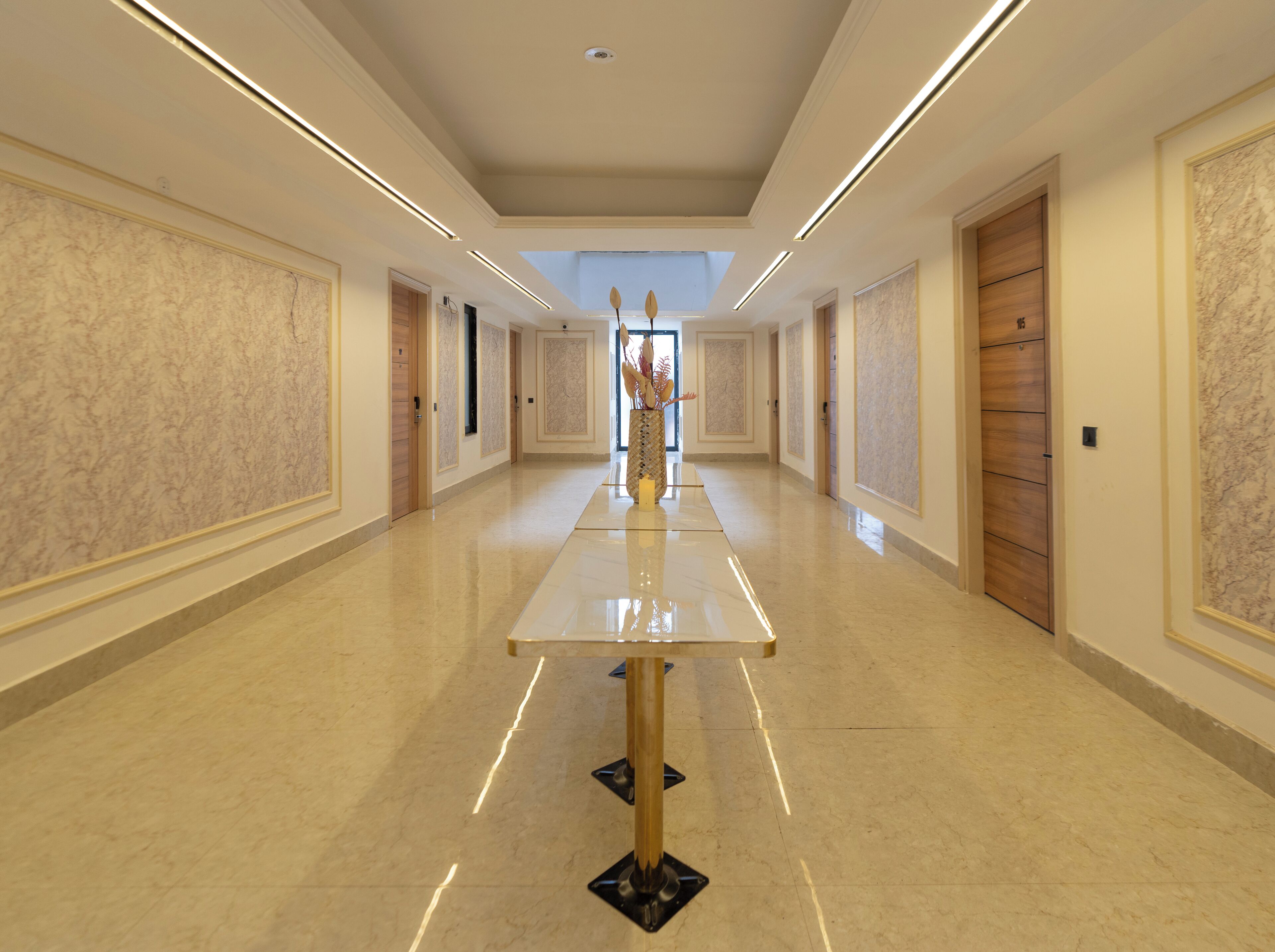 A long, well-lit hallway with marble walls and doors, leading to a central area with a decorative vase.