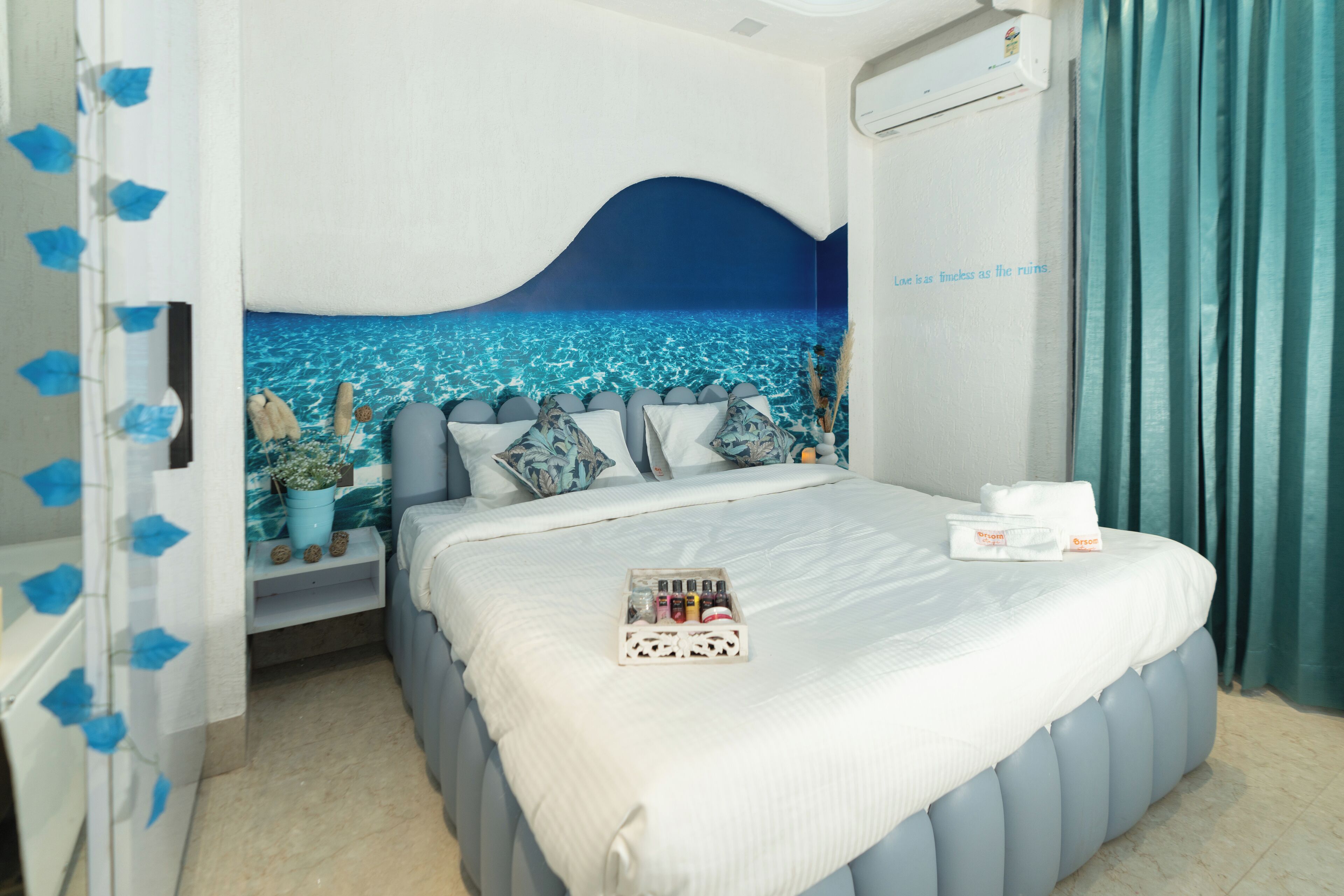 A bedroom with a bed, a nightstand, a wall mural, and a window with curtains.