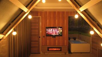 Ein gemütliches Schlafzimmer im Dachgeschoss mit Fernseher, Kamin und Badewanne.
