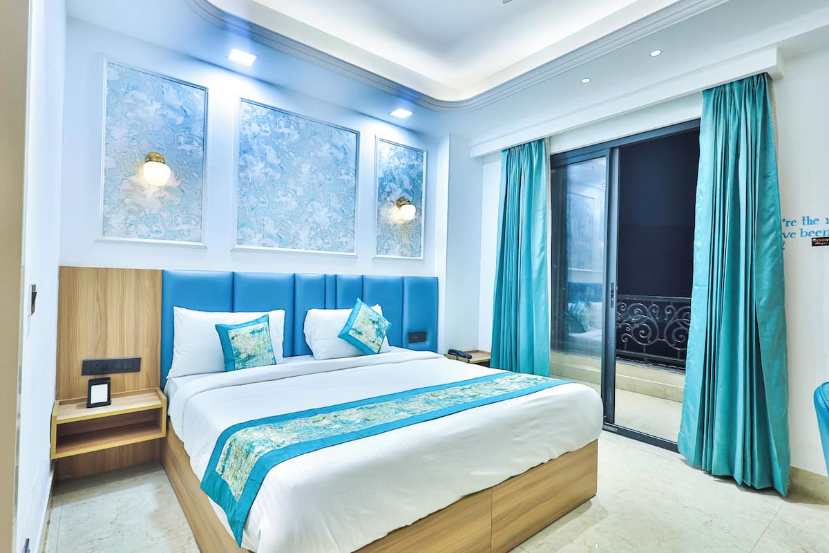 Une chambre moderne avec un grand lit, une table de chevet, une lampe fixée au mur et une vue sur le balcon extérieur.