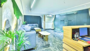 A modern lobby with a seating area, a reception desk, and a green wall. - Orsom Stays Sassy Sector 53 (Gurugram)