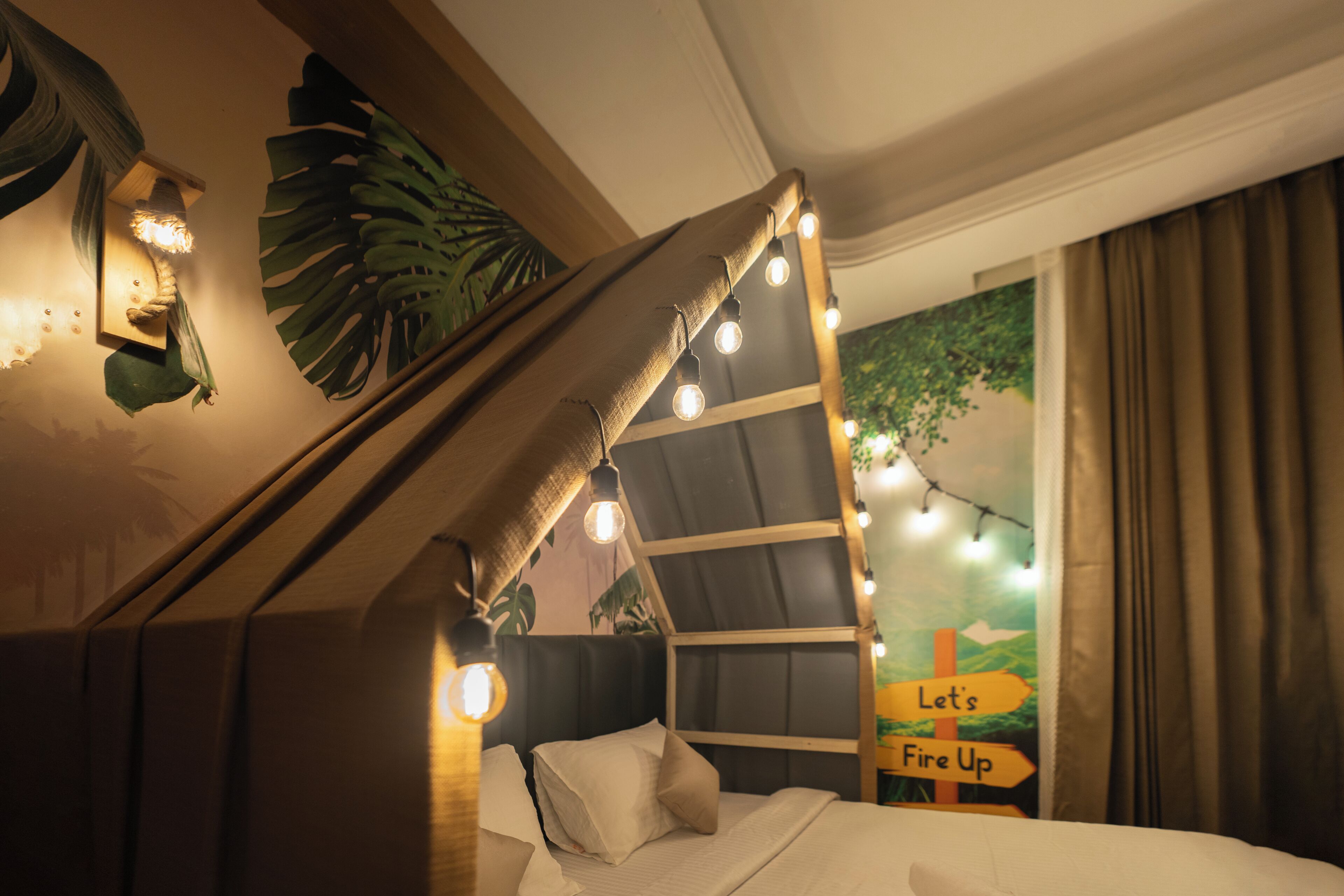 A bed with a headboard, a wall-mounted light fixture, and a sign that reads "Let's Fire Up".