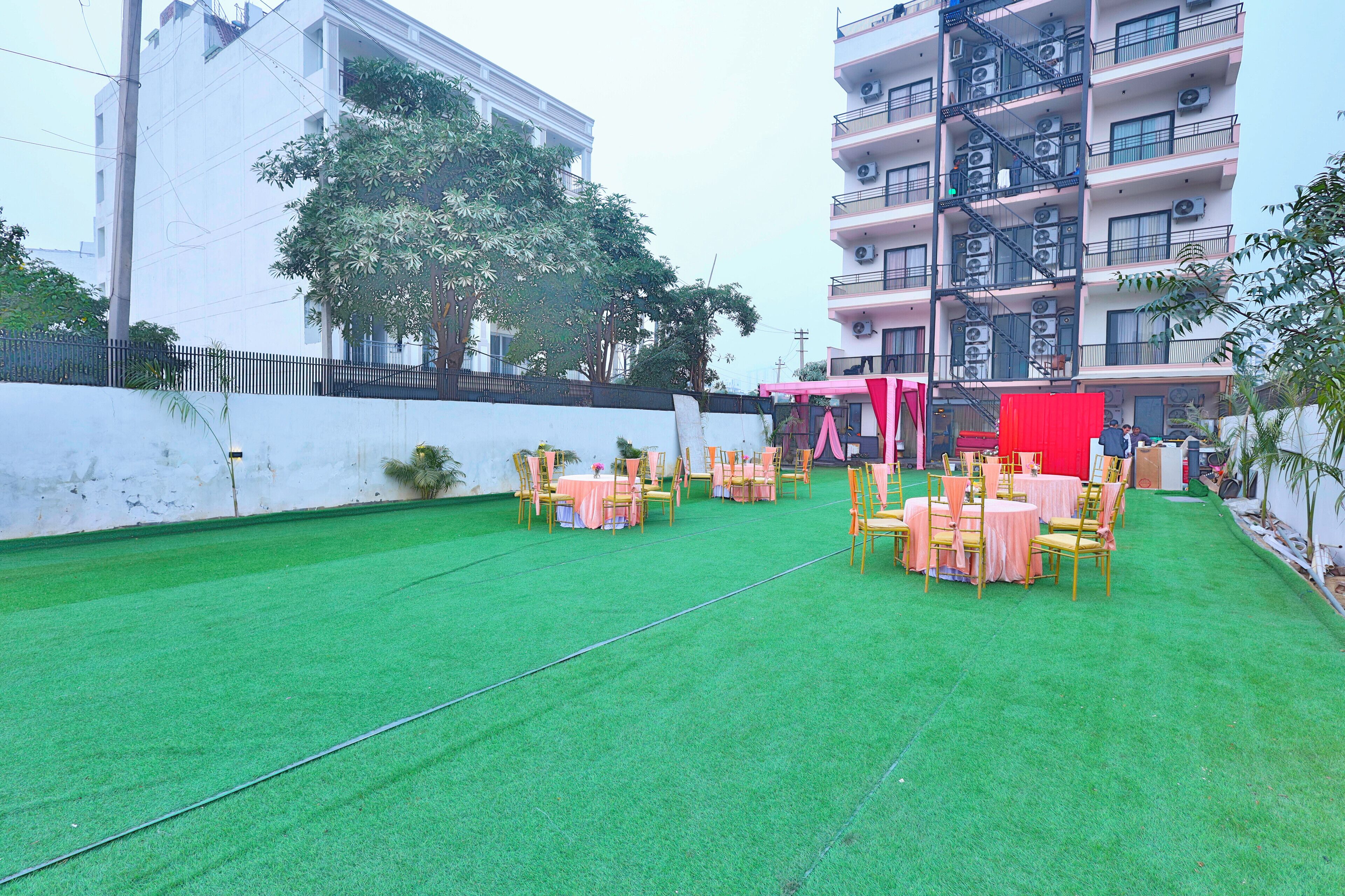 An outdoor area with artificial green turf, tables with chairs, and a red backdrop.