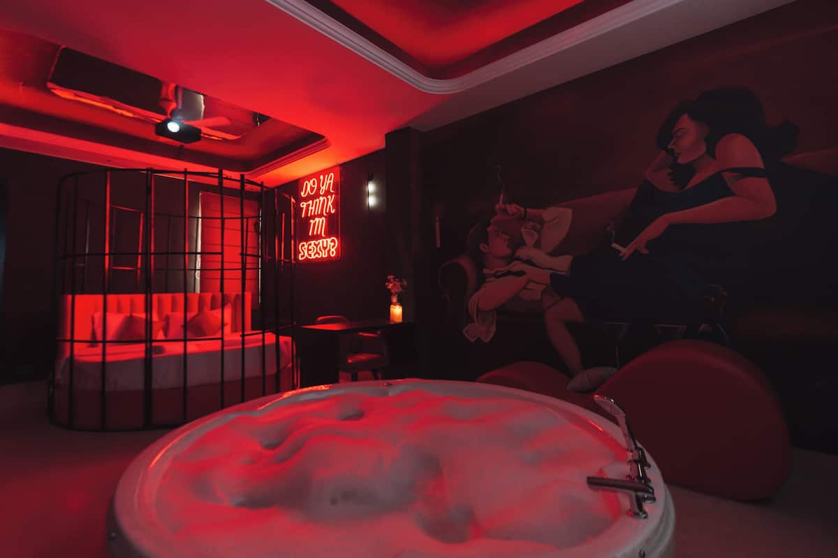 Une pièce avec un bar éclairé de lumière rouge, un jacuzzi rond et une fresque représentant une femme.
