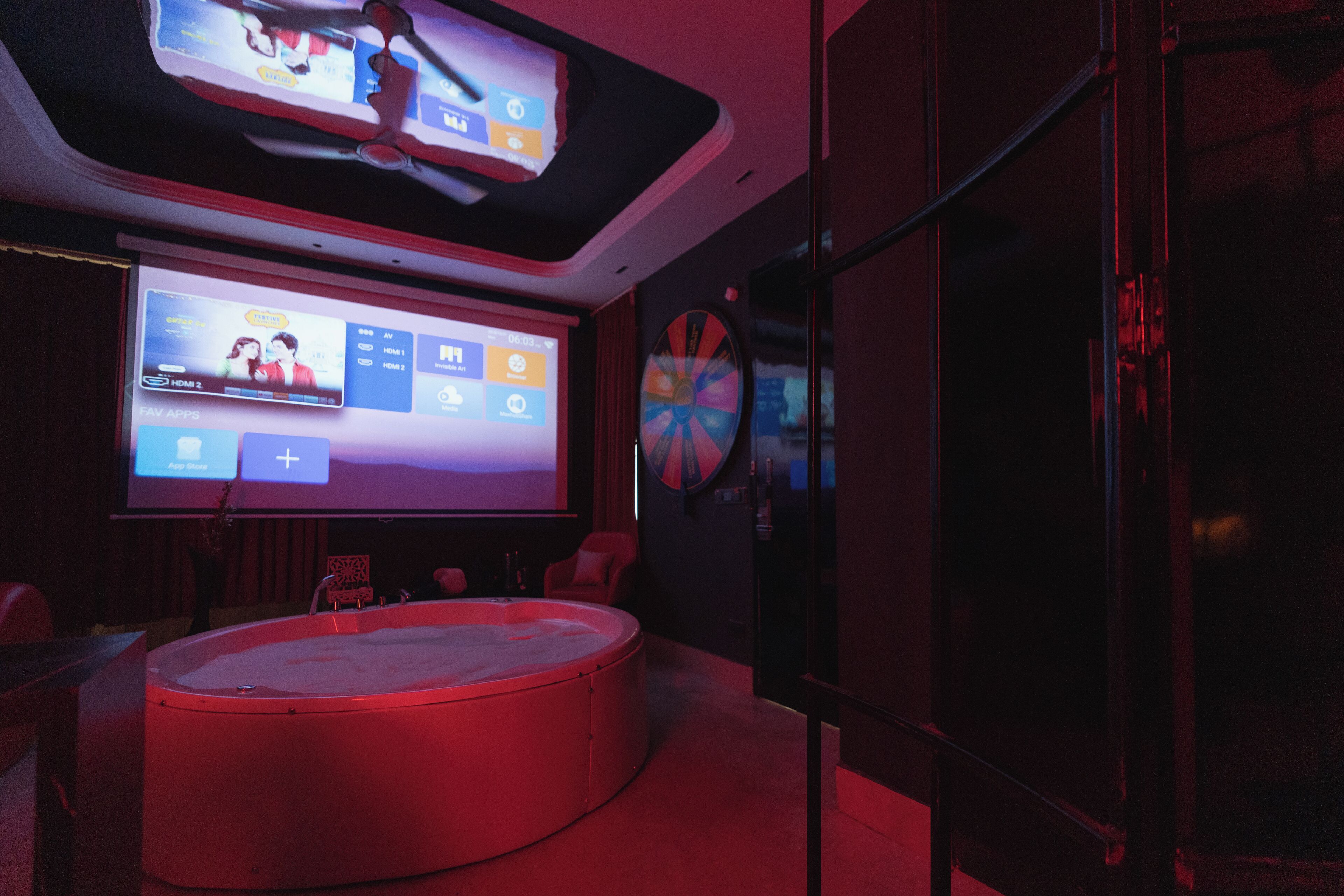 A modern room with a large screen displaying a movie and a circular seating area with a red ambient light.